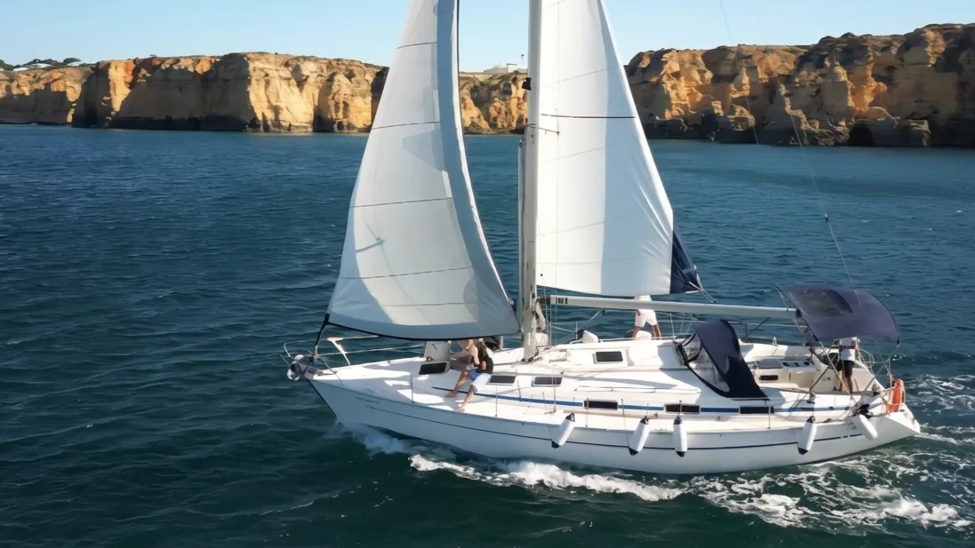 Iate privado à vela com passageiros a bordo junto às falésias de Lagos, Algarve